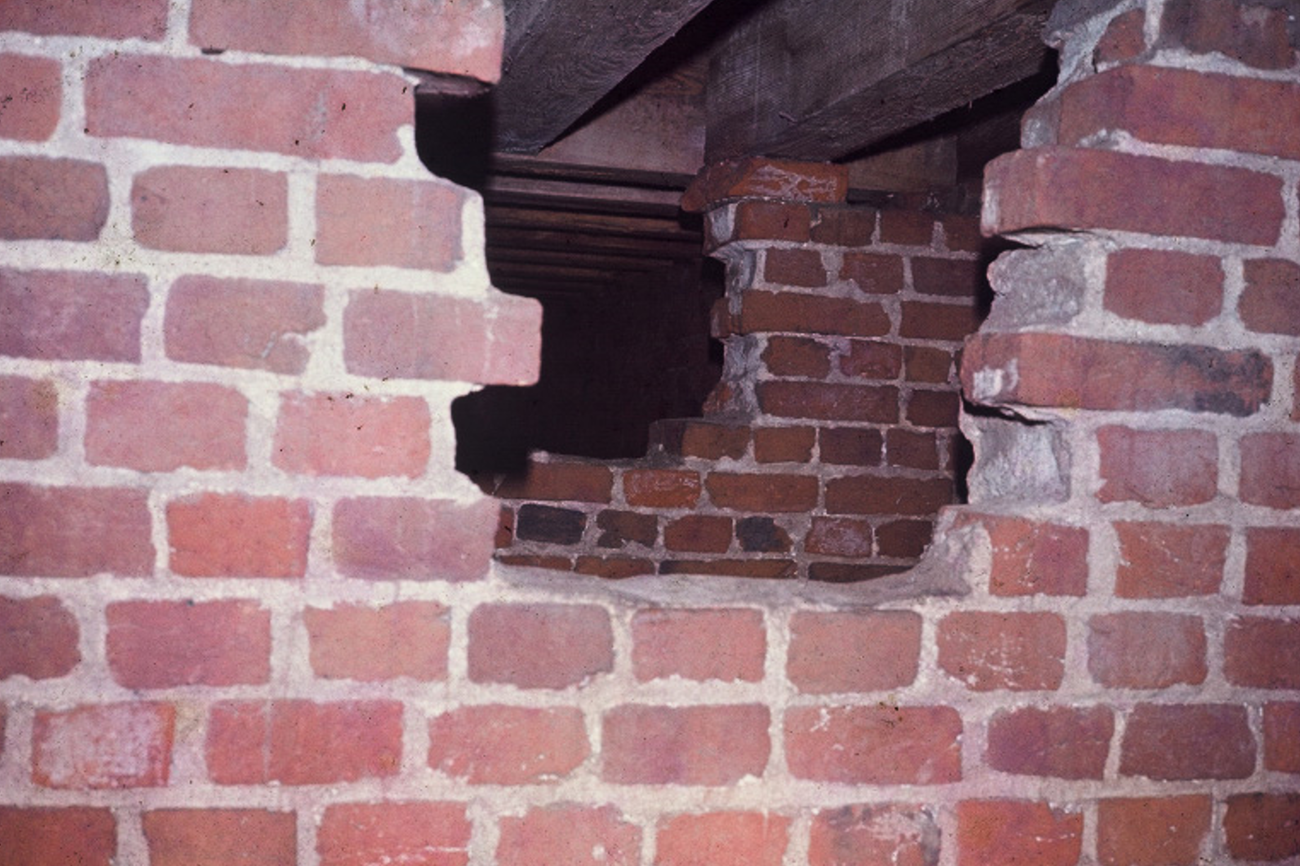 Large holes in two brick walls in a crawl space under a wooden floor.