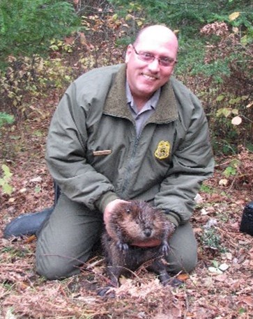 Photograph of person kneeling and holding beaver in the forest.