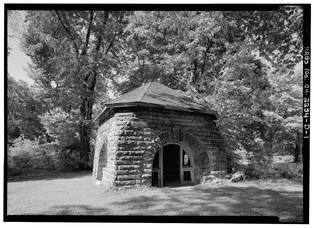 The stone pumphouse and windmill base before reconstruction, with arched doorways and a shingle roof
