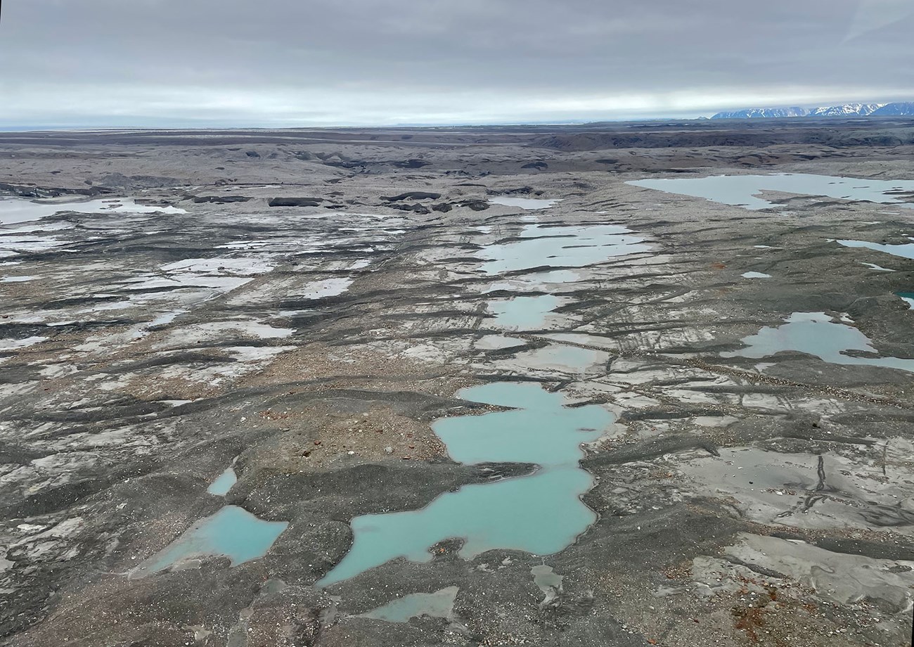 The debris-covered surface of a glacier with small pools of water.