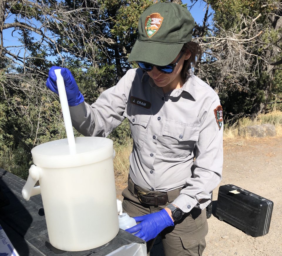A scientist in an NPS uniform filling small plastic bottles with water from a larger container on the tailgate of a truck.