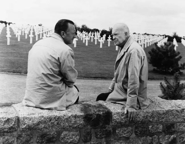 A black and white image of two men sitting on a stone wall