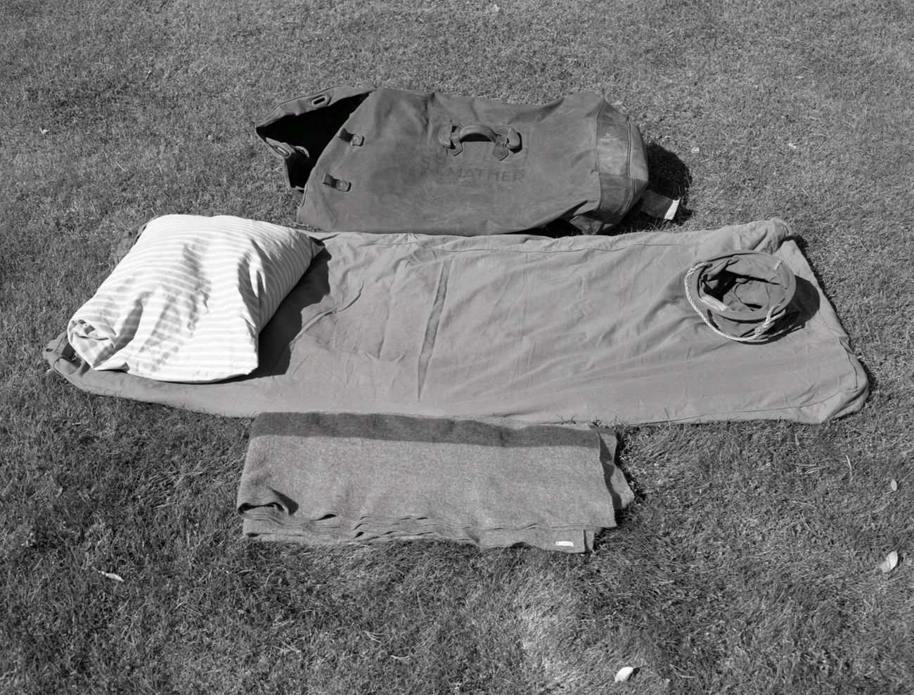 Deflated mattress, blanket, pillow, bag, and bucket on ground