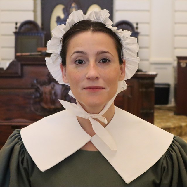 woman in a bonnet and wearing a plain dress with a white quaker collar.