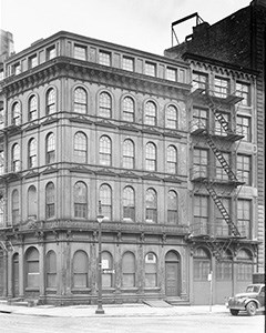 Five story cast-iron building with arched window frames and a fire escape stairs on the side