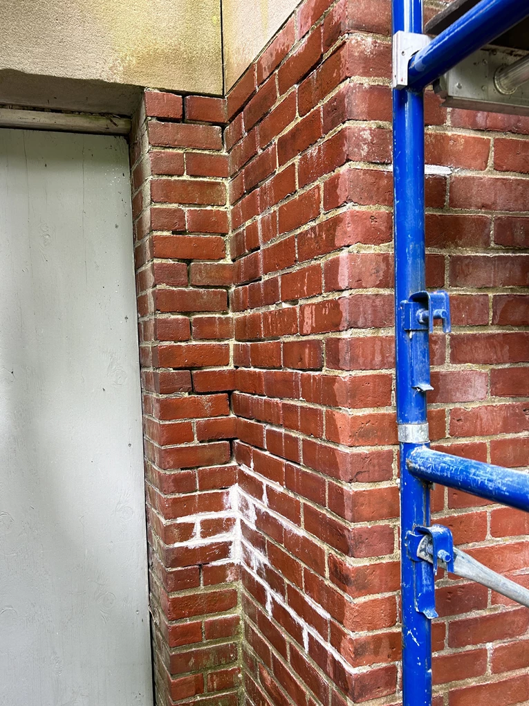 A corner where two old brick walls meet. Much of the mortar has crumbled, leaving empty spaces between the bricks.