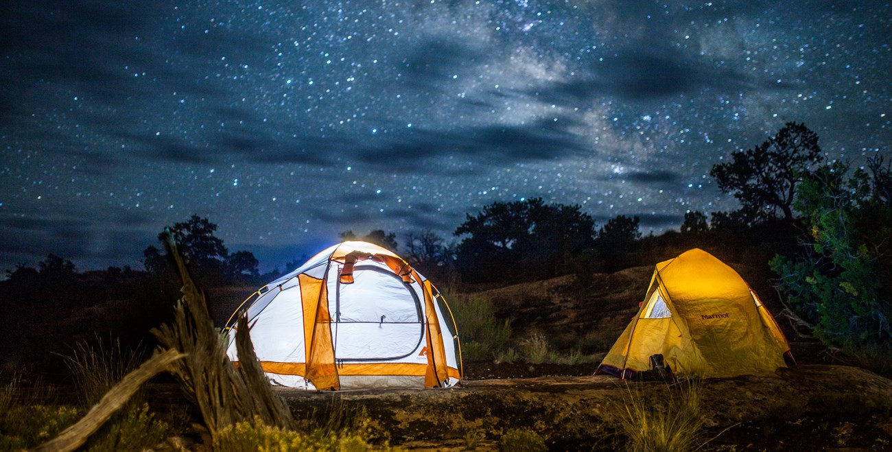 two tents are lit up under a starry night sky