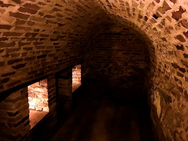 A vaulted room made of brick with small storage shelves built into the brick. The dark area is illuminated by soft candle light.