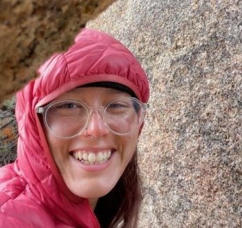 Woman standing near rock wearing a hooded down coat and smiling.
