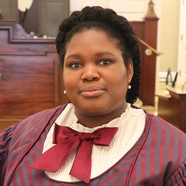 portrait of a black woman with hair neatly tied up and wearing a dress with a red bow on the collar.