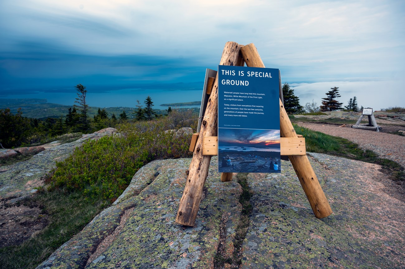 A wooden three-legged display on a granite boulder on a mountain summit