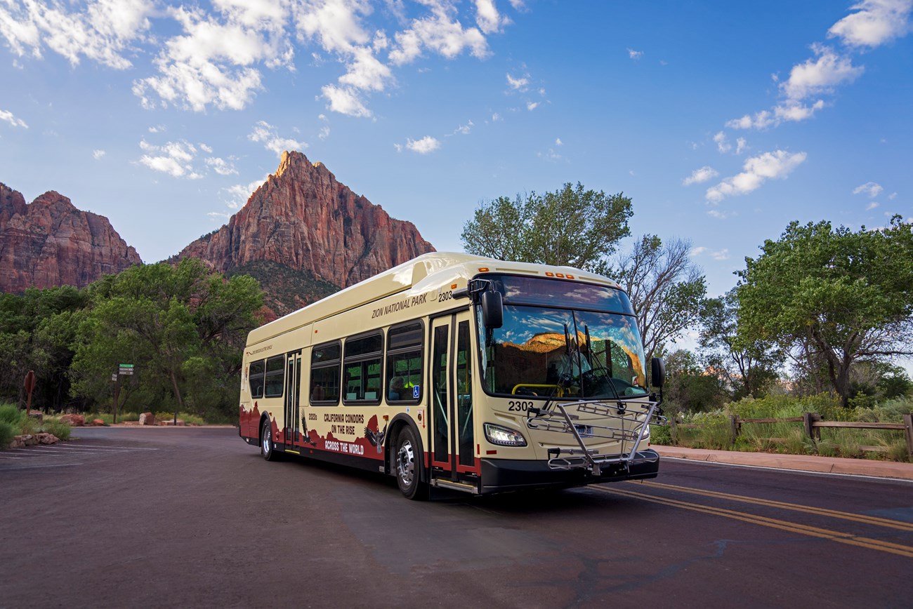 an electric shuttle bus in a parking lot with beautiful sandstone mountains in the background