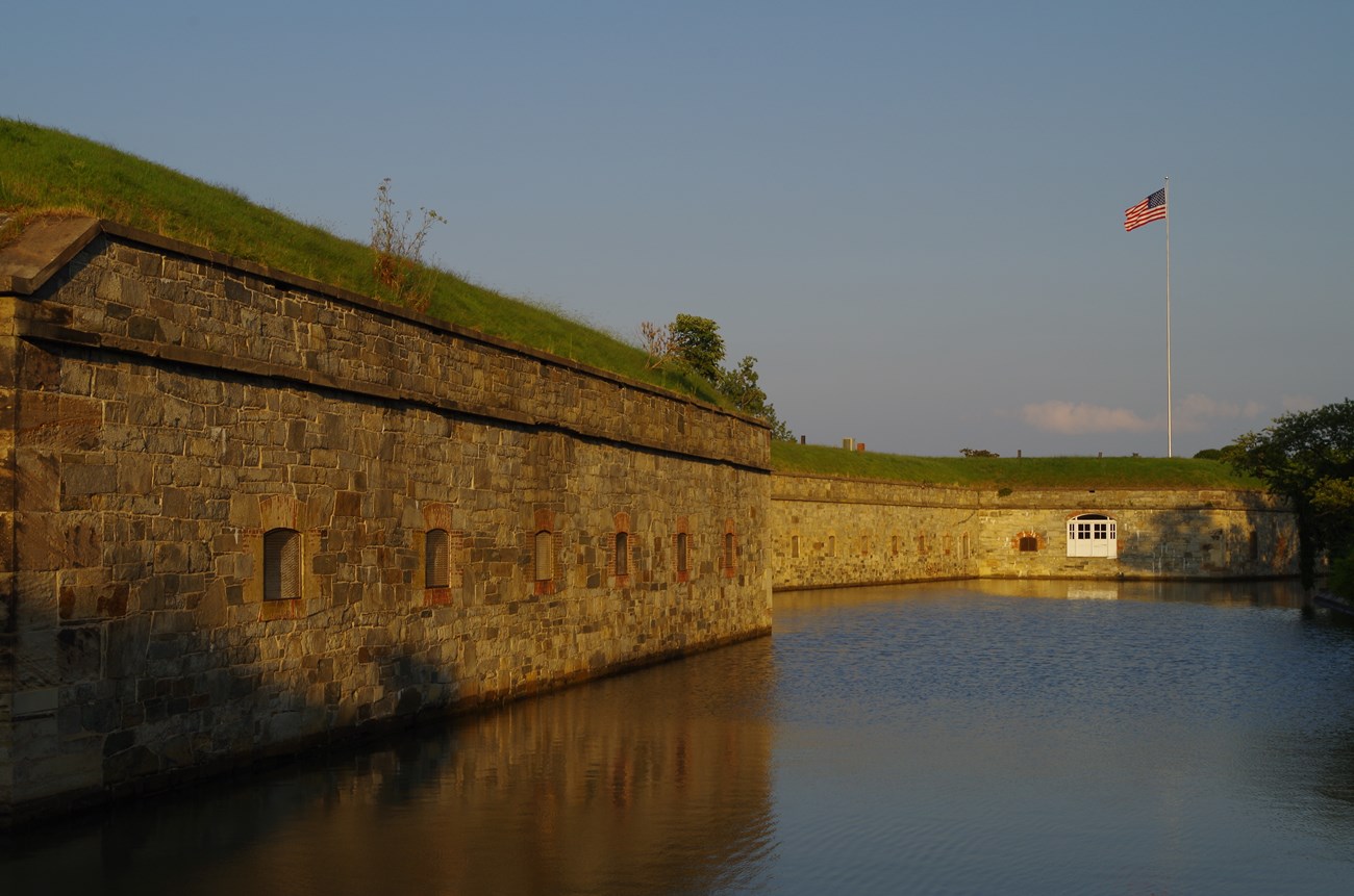 The setting sun lights a stone fort wall where a US flag flies high