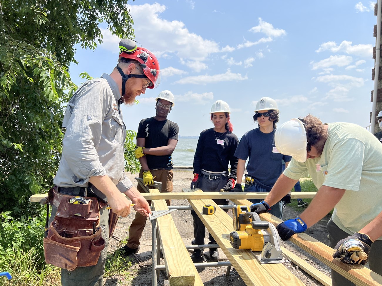 A group of people stand outside wearing hard hats and surround a circular saw