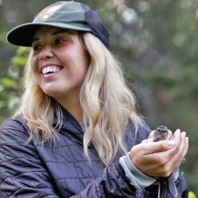 A woman smiles and holds a small gray bird in her hands