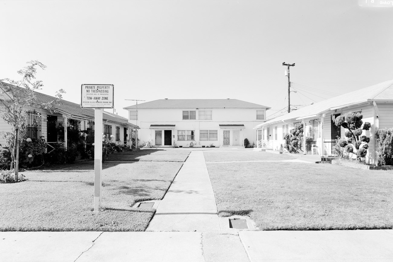 Modest white clapboard single-storey homes around a grassy courtyard, with a sign reading "private property no trespassing"