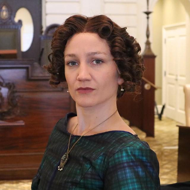 portrait of a woman with parted curly hair pulled back wearing a patterned dress.