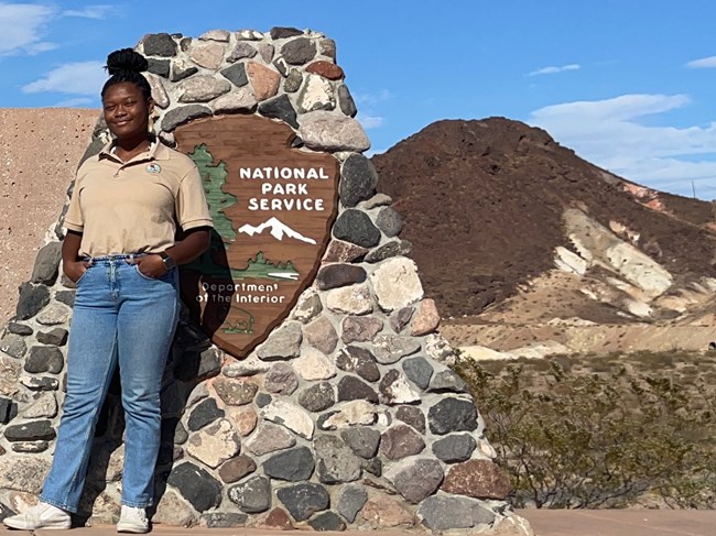 Woman wearing jeans and internship T-shirt smiling near Lake Mead National Recreation Area sign.