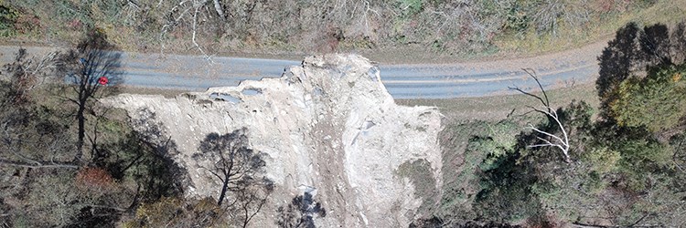 Aerial view of forest and road where a landslide has obliterated a section of road.