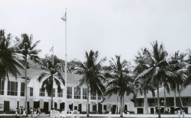 People play under palm trees in the courtyard of a large white house.