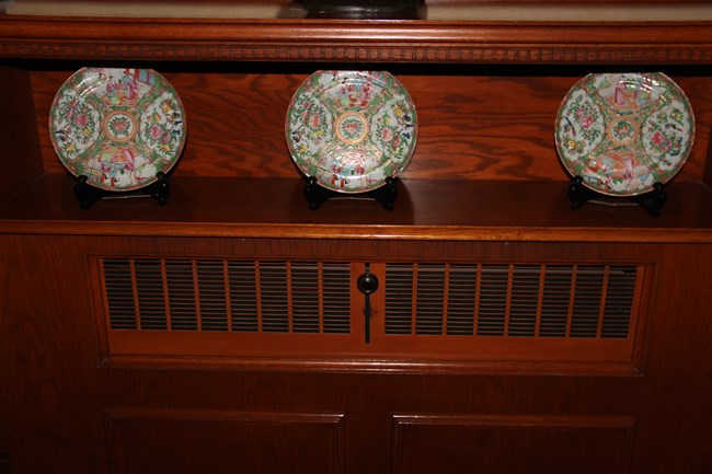 Three Famille Rose plates displayed on a shelf in the Mansion’s hallway.