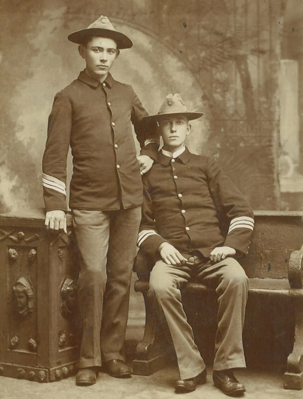 A black and white image of two men in a portrait studio wearing military uniforms. Christopher Ambrose Dunnigan is a young man with dark hair.