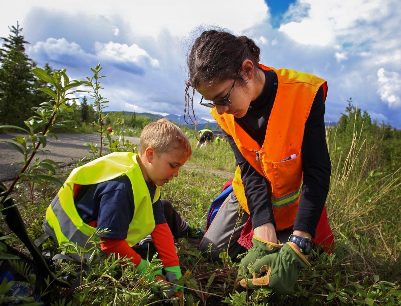 a young boy and girl in high visibility vests pull weeds