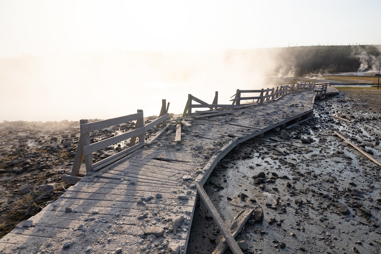 a damaged boardwalk covered with rock and debris in a hydrothermal area