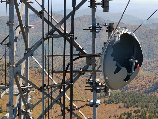 Communication tower with damage against a backdrop of mountains with colorful autumn trees.