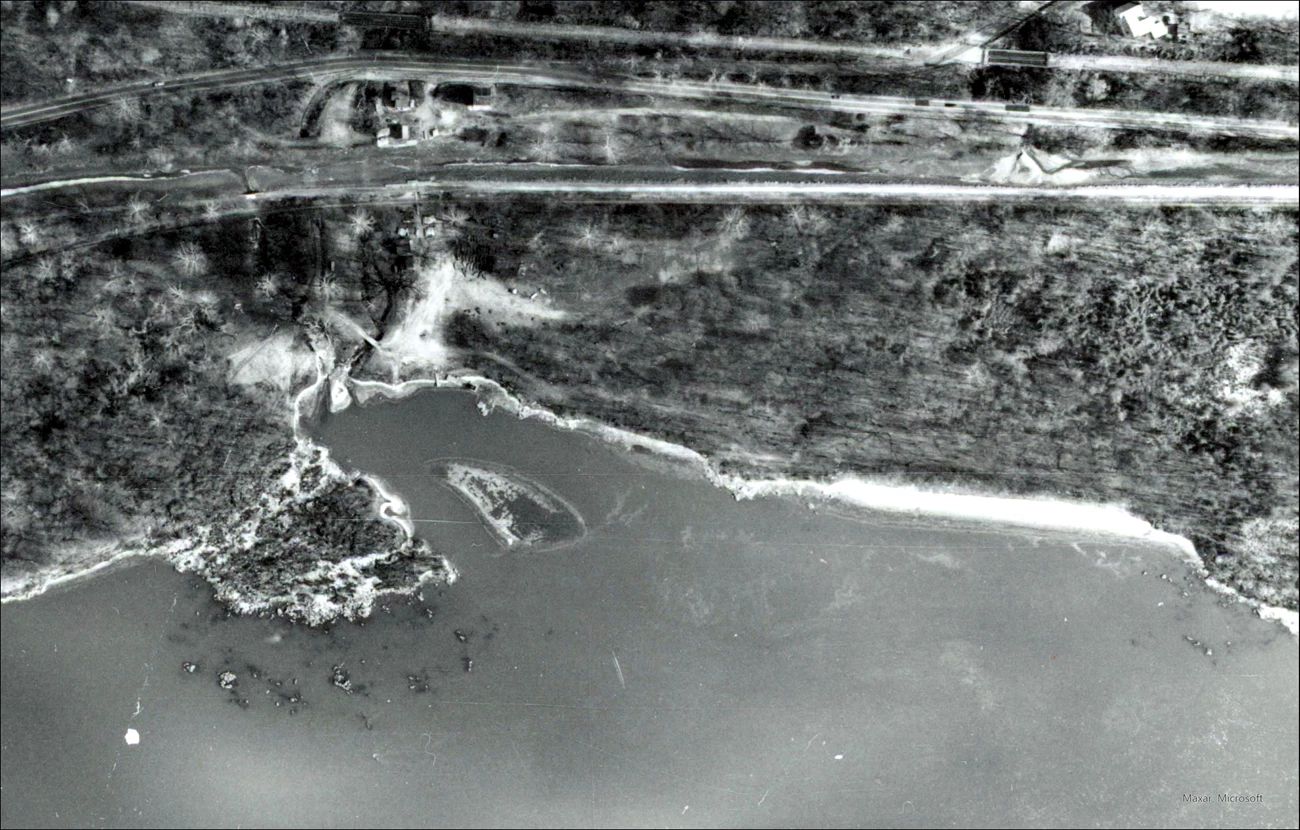 Black and white aerial photo of Fletcher’s Cove that shows a wide worn area in place of the previous dirt path from the boathouse to the Potomac River. The Potomac River is at the bottom of the image and the Chesapeake and Ohio Canal is towards the top.