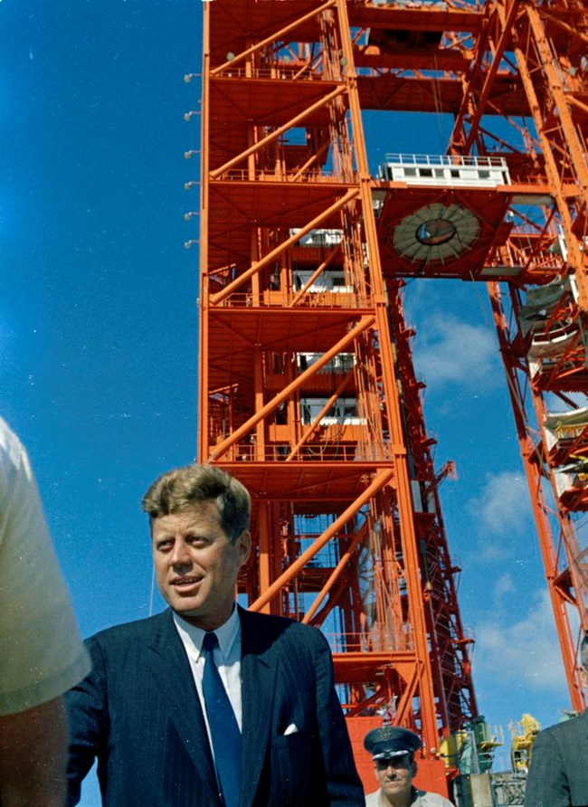 Kennedy is shown with towering red scaffolding behind him