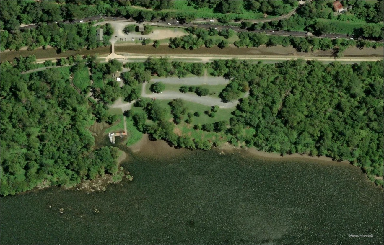 Black and white aerial photo of Fletcher’s Cove that shows a wide worn area in place of the previous dirt path from the boathouse to the Potomac River. The Potomac River is at the bottom of the image and the Chesapeake and Ohio Canal is towards the top.