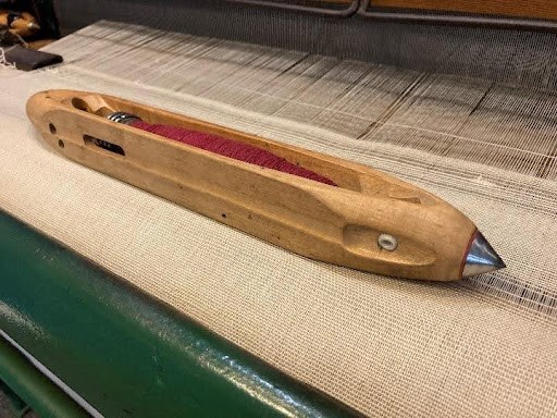 A wooden shuttle on a power loom