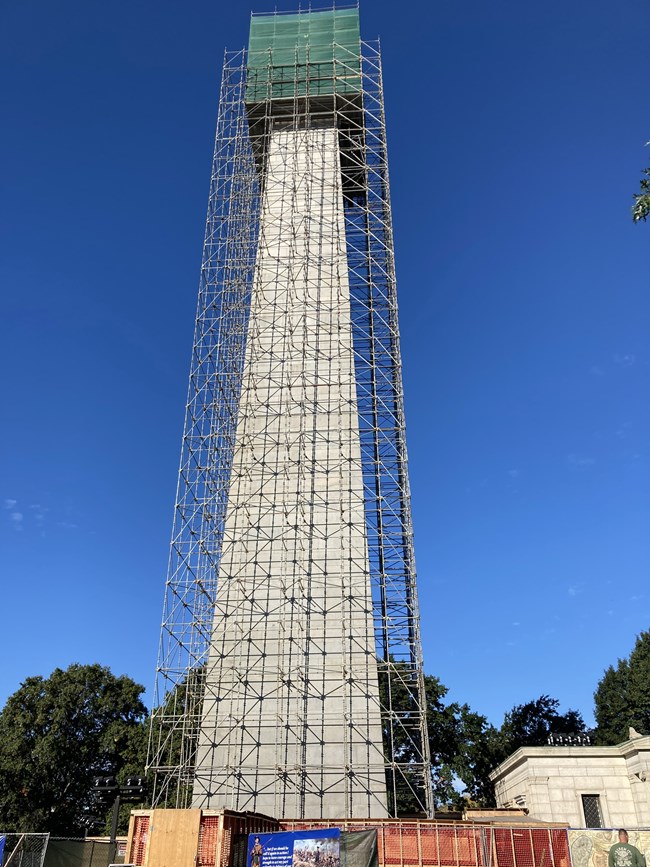 The monument wrapped in steel scaffolding, its top covered in green mesh
