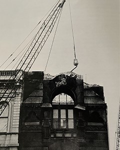 Tall building being torn down with a crane and wrecking ball in the background.