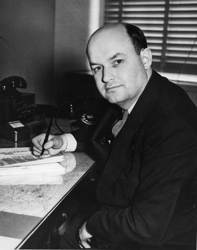 Ronald Lee sitting writing at his desk, looking towards the camera