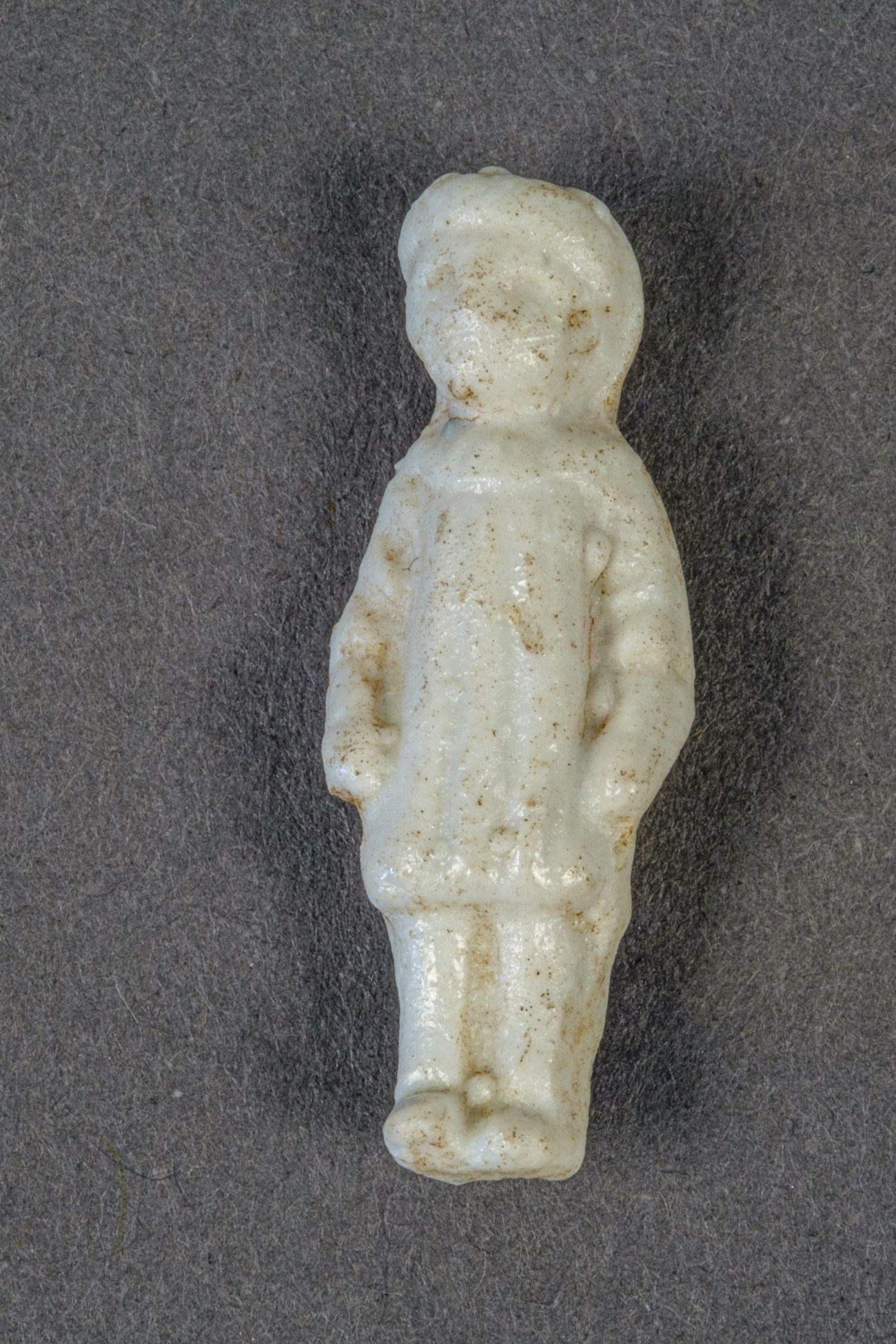 A small white ceramic doll with Victorian style clothing and a face void of expression or remorse