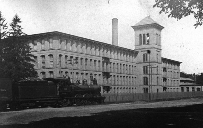Train in front of large 4-story brick mill