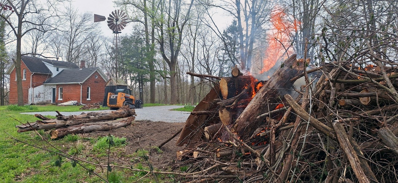 Flames consume dead logs in a pile near a brick structure.