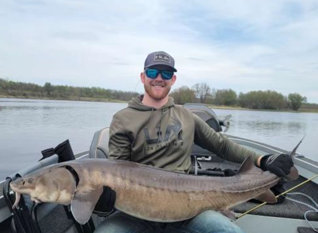 Photograph of person in a boat holding a large fish.