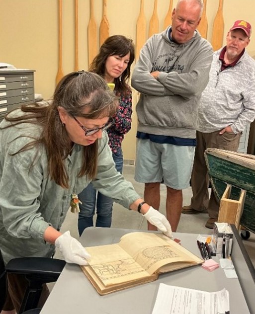 Photograph of person wearing gloves and opening old book with people looking.