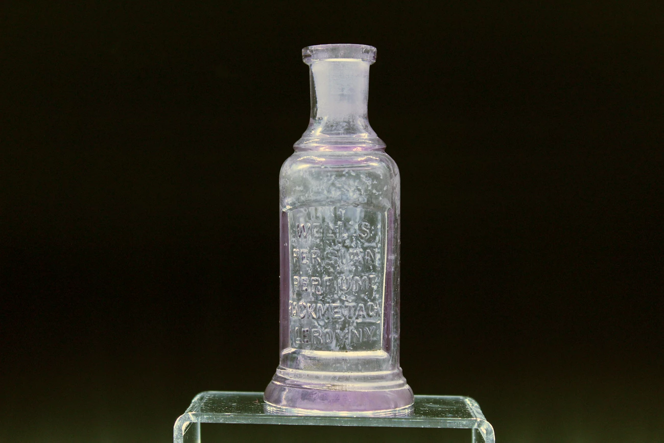 Small glass bottle with inscription sits on acrylic stand.