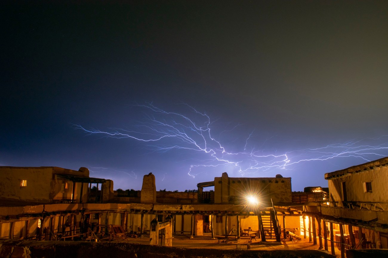 A night sky with streaks of lightning is above the adobe fort.