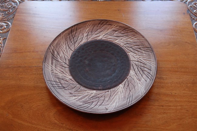 One brown stoneware plate with twig details on a coffee table in the Mansion Parlor.