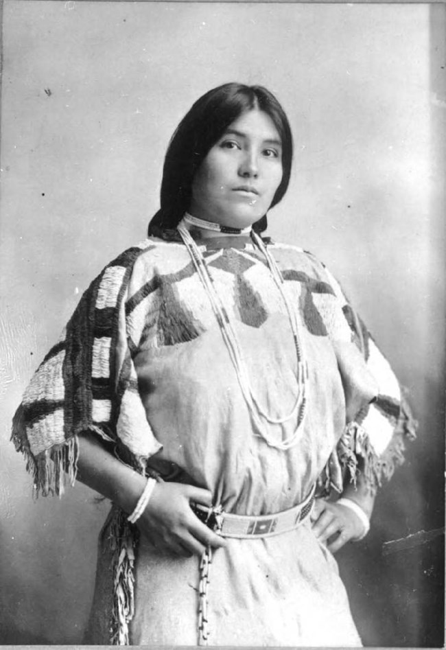 Black and white portrait of a young Indigenous woman in a beaded dress and belt